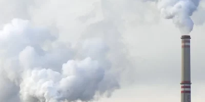 Sur cette image, nous voyons des fumées et des usines. L'image a pour but de représenter l'appel à projets Première Usine du plan investissement de France 2030.